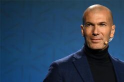 زين الدين زيدان يرتدي بدلة رسمية ويقف أمام شعار منتخب فرنسا